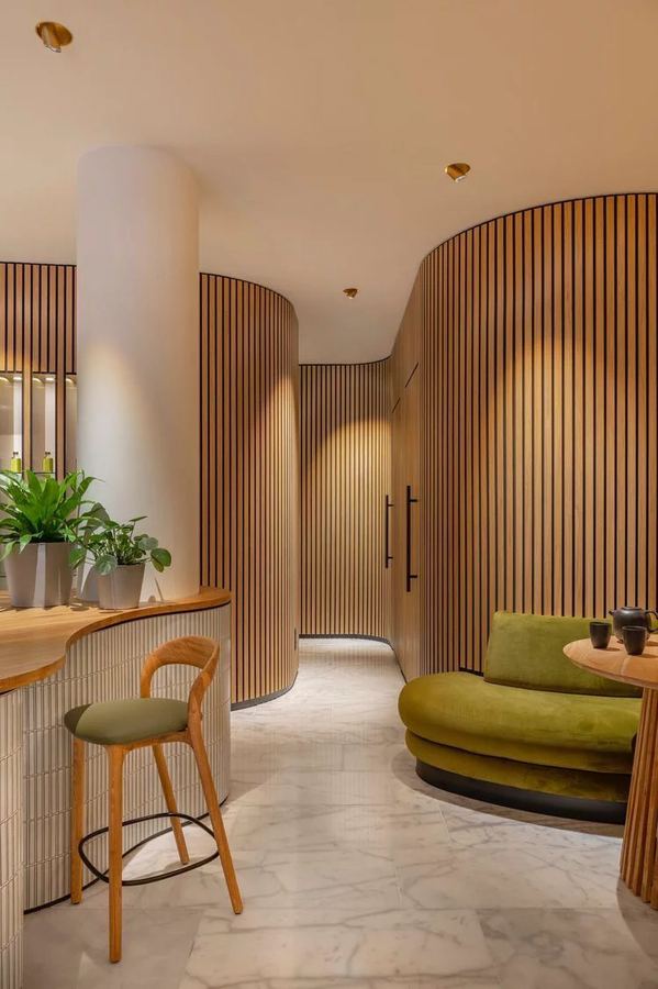 Curved wood-slatted wall with a concealed door identified only by a vertical blackened-steel pull, warm interior